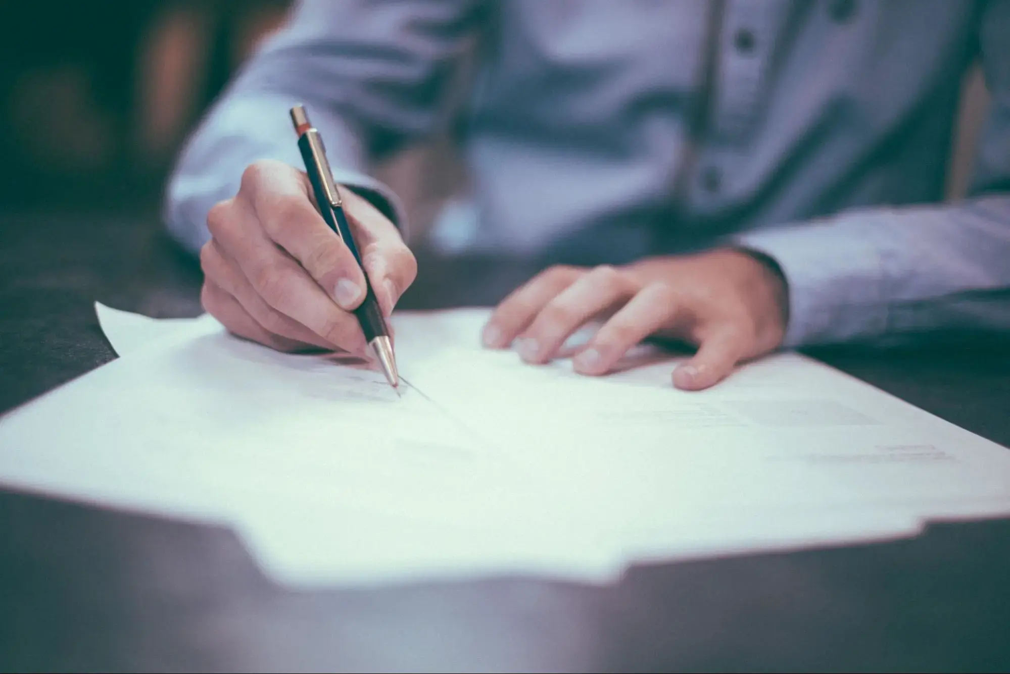 A person signing a document to gift their life insurance policy to a charity.